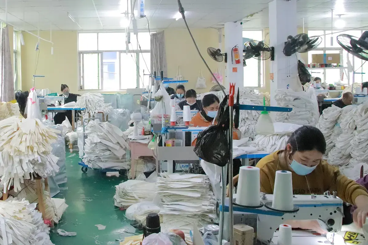 Masked workers sewing tote bag panels in a production workshop.