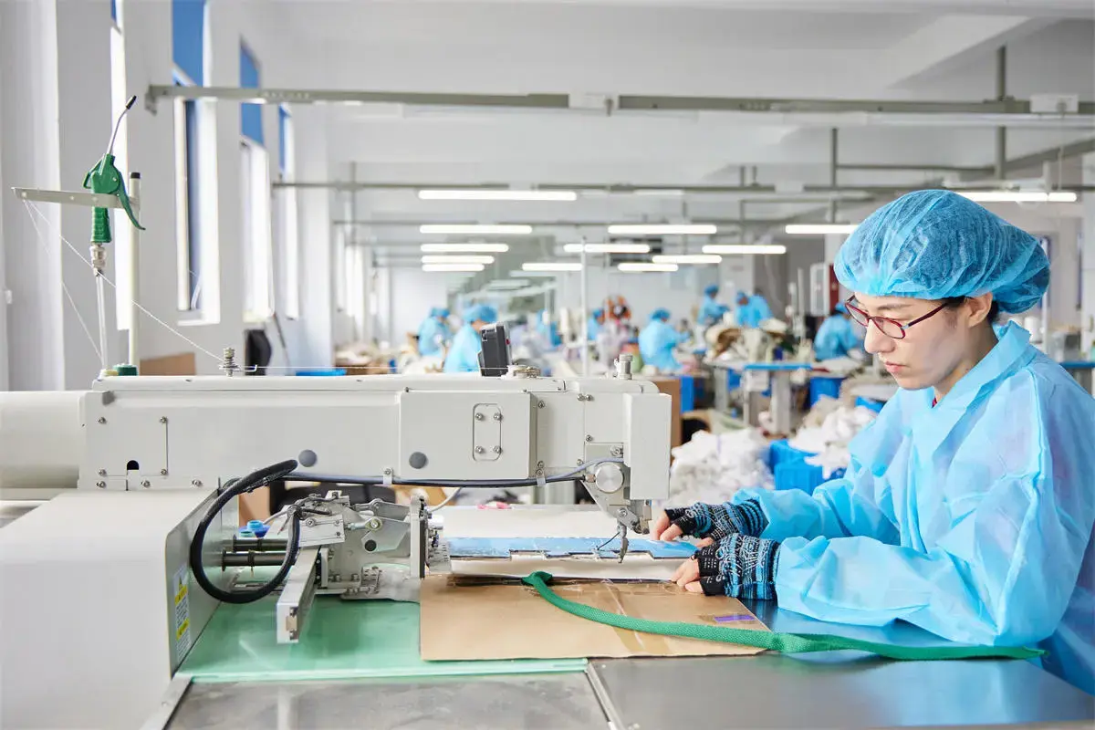 Uniformed operator sewing and checking a tote bag material panel.