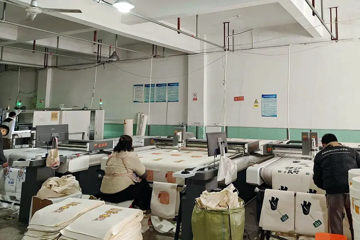 Operators producing printed tote panels on large-format factory equipment.