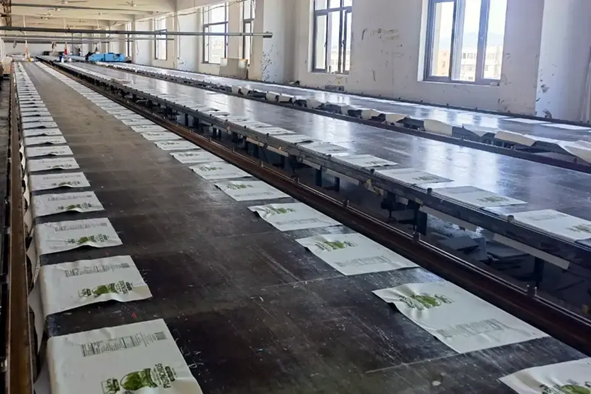 Rows of printed tote bag panels arranged on long screen-printing tables.