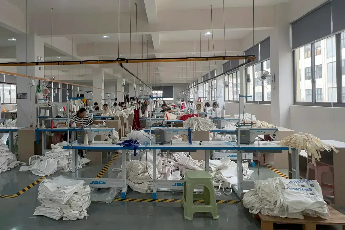 Workers sewing natural tote bags across a bright production workshop.