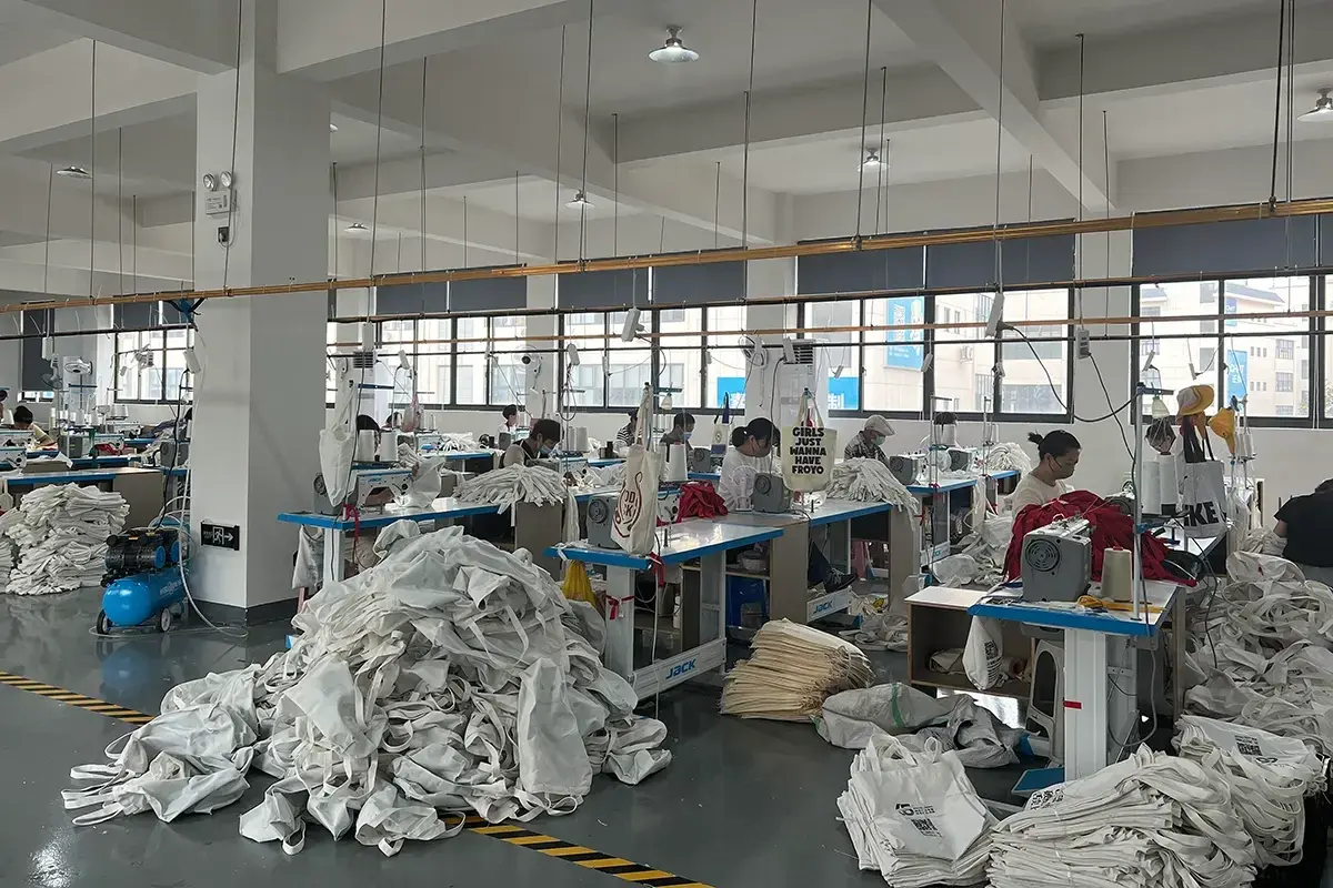 Cut fabric pieces collected beside tote bag sewing stations.