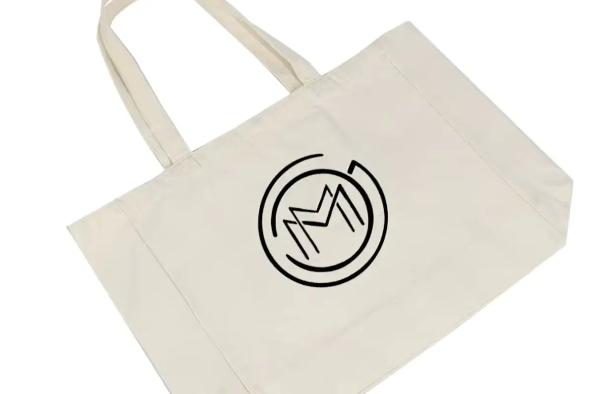 Black circular artwork on a white canvas tote bag.