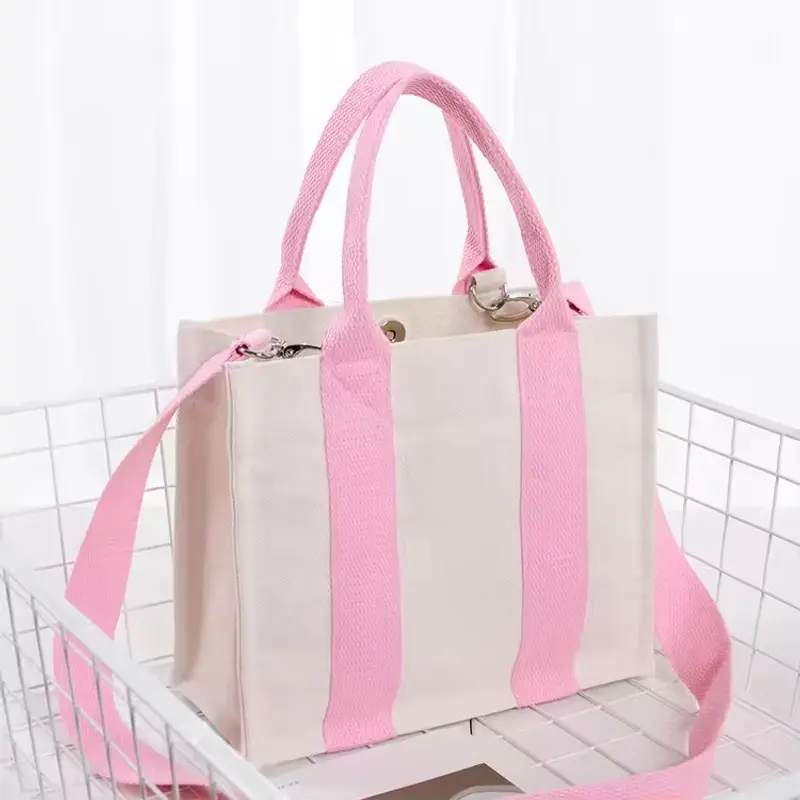 Cream canvas tote bag with pink webbing handles and shoulder strap.
