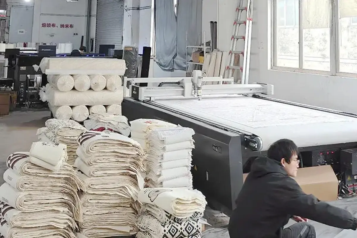 Cut cotton tote panels stacked beside an automated cutting table.