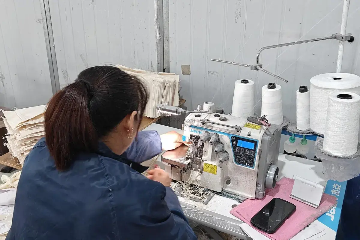 Worker finishing cotton tote panels at an industrial overlock machine.