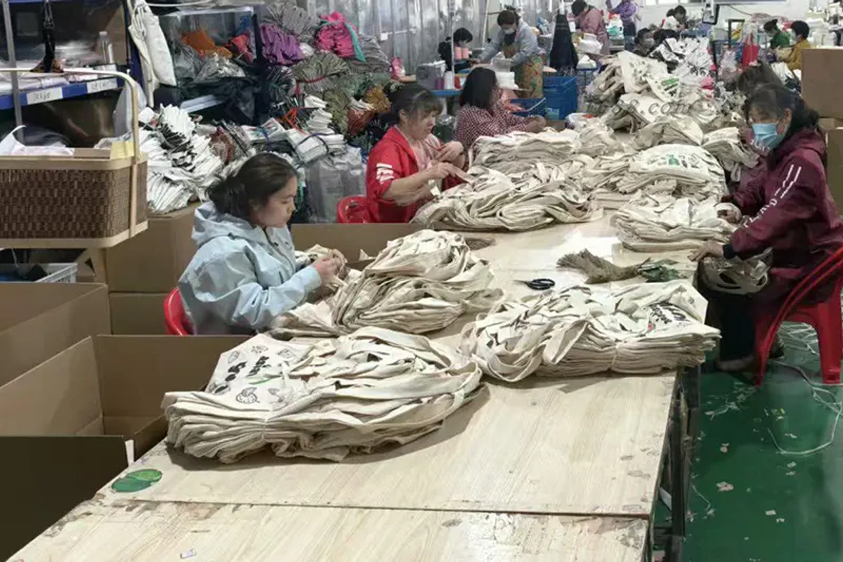 Workers sorting stacks of finished natural cotton tote bags.
