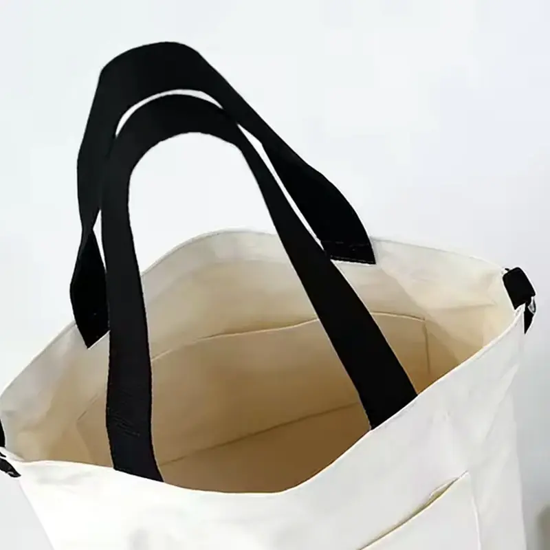 Open white canvas tote showing its interior pocket and zipper hardware.