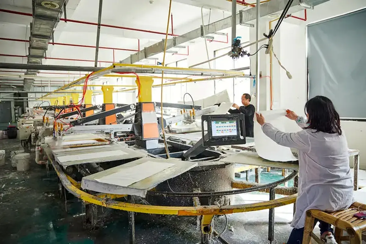 Operators running fabric panels through automated production equipment.