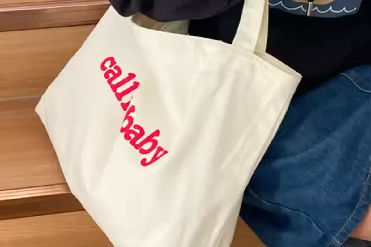 White canvas tote with black handles and pink printed lettering