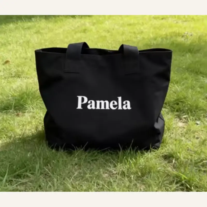 Black gusseted canvas tote bag standing on grass