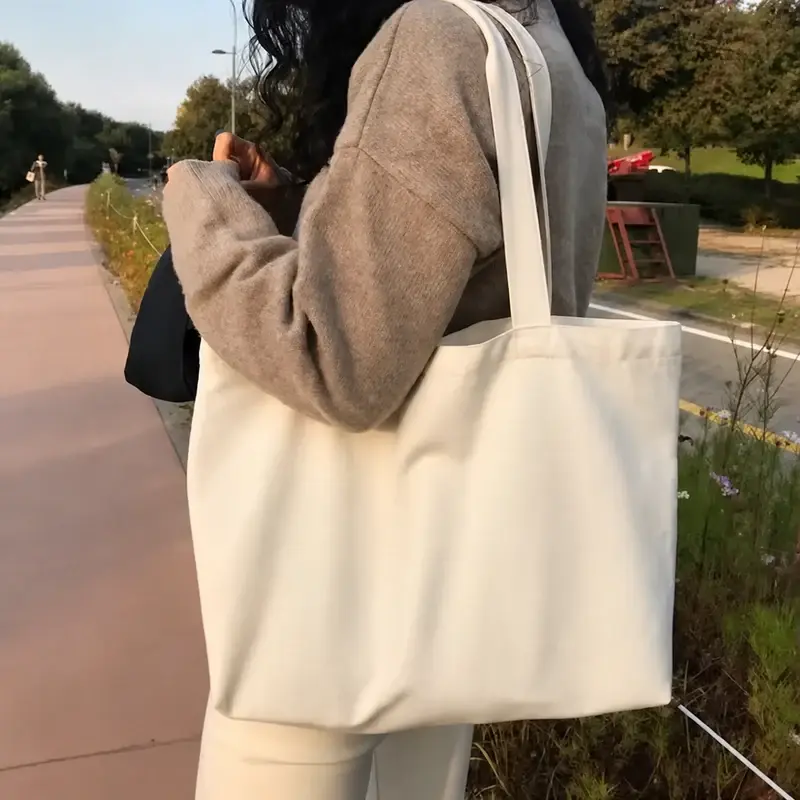 Blank natural canvas tote bag carried on an outdoor path