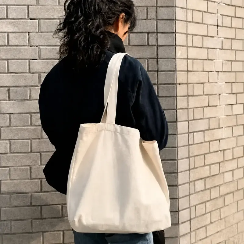 Blank natural canvas tote bag carried beside a brick wall