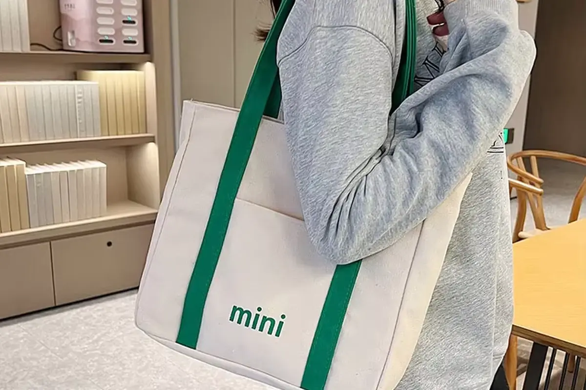 Natural cotton tote with green trim shown in shoulder carry