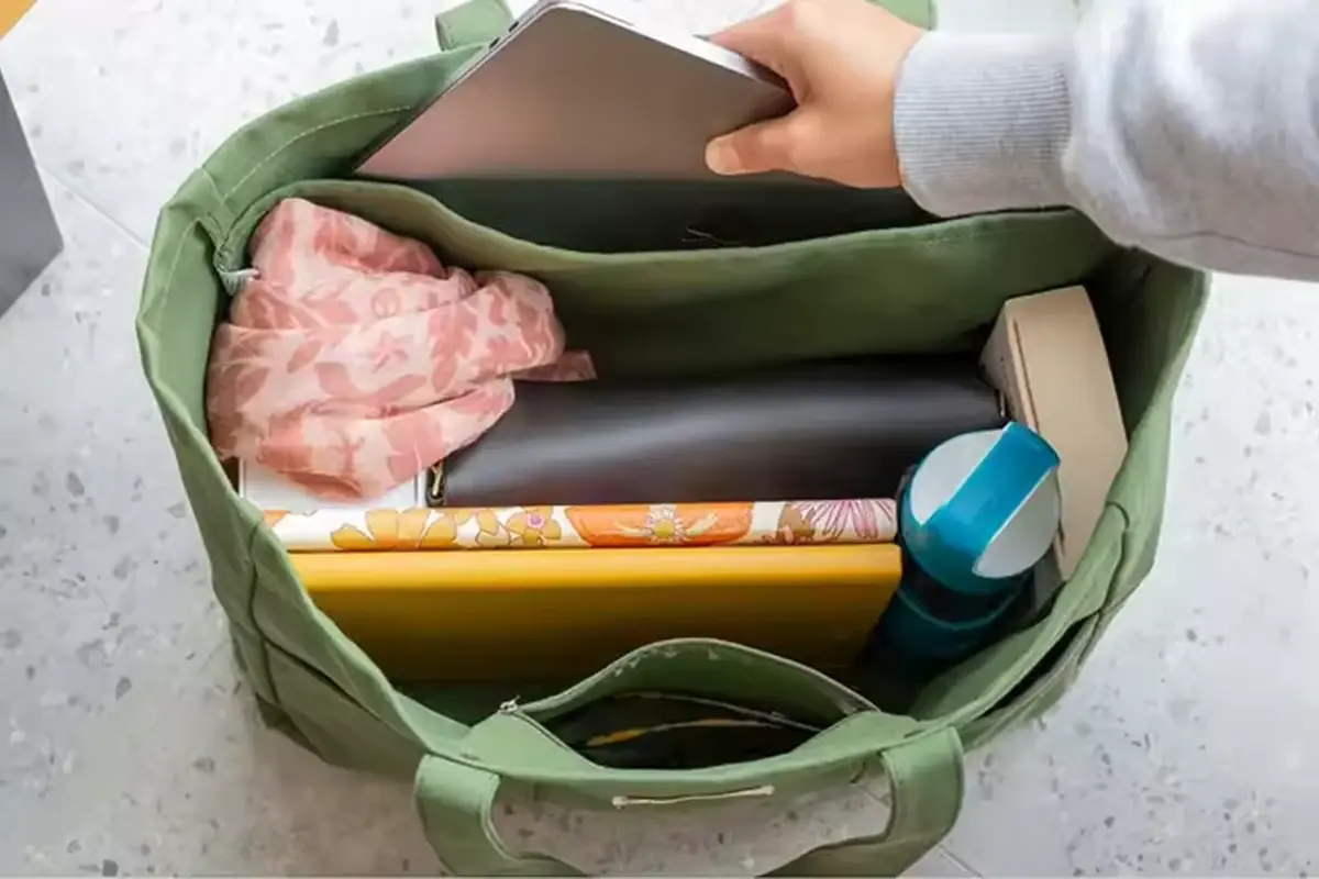 Open green canvas tote packed with books a tablet and bottle