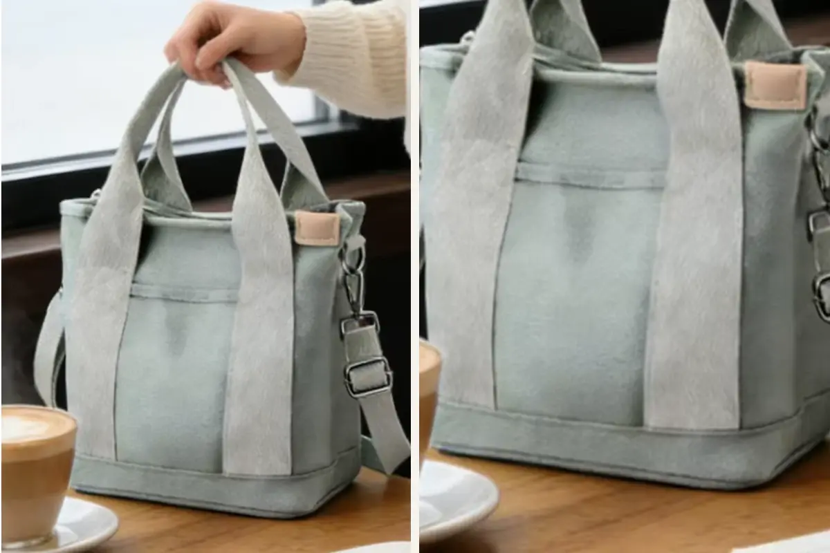 Sage canvas zipper tote carried by hand beside a cafe table